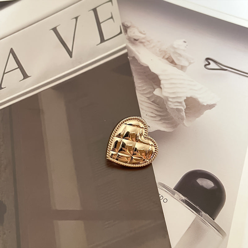 Botón corazón metálico dorado brillante, borde trenzado, relieve facetado y pasador trasero