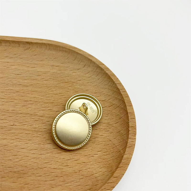 Matte gold round metal shank button with serrated edge, showing back view