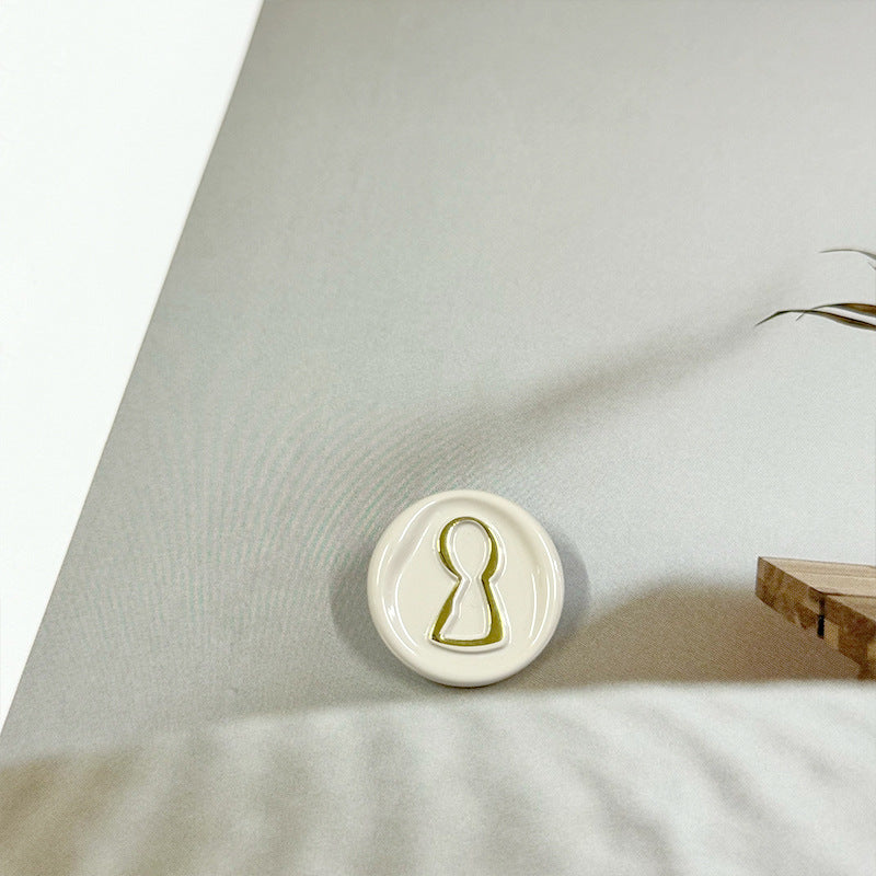 23mm round button, white with golden-lined miniature figure icon on the face