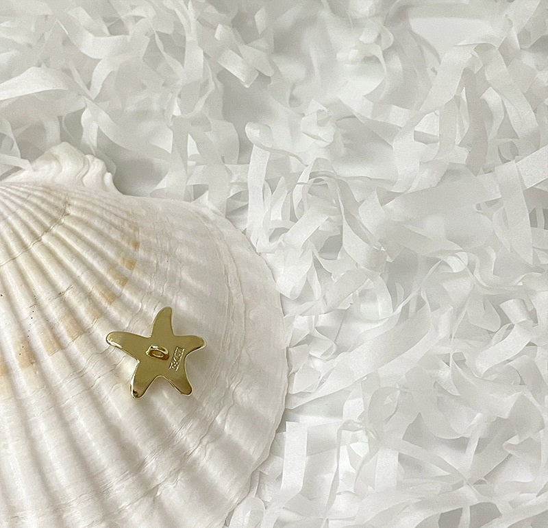 Gold starfish-shaped rhinestone metal shank button on white fabric