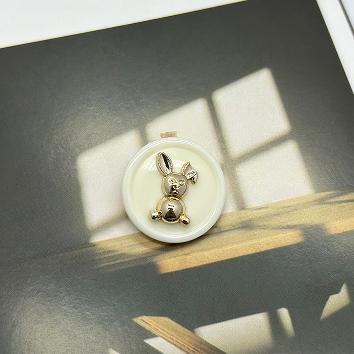 Beige-gold rabbit round button with metal rabbit centerpiece on cream resin base.