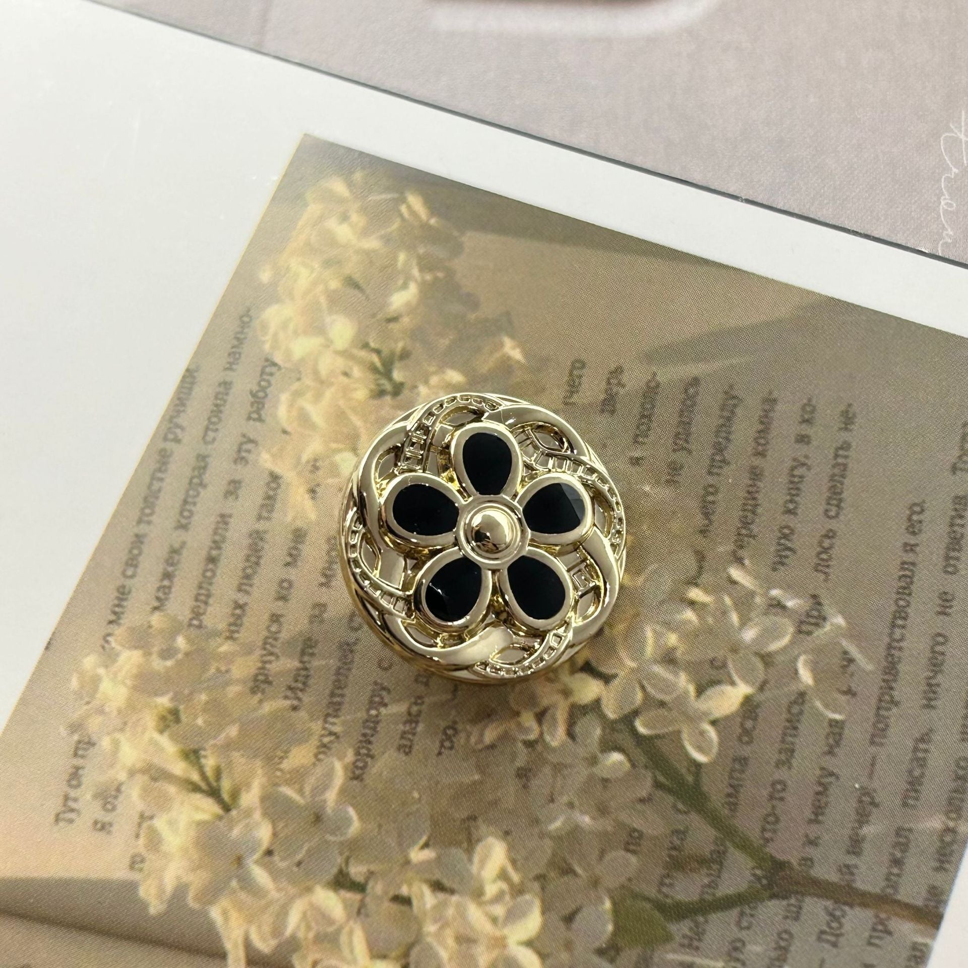 Round metal button, gold-tone floral lace design with black enamel petals