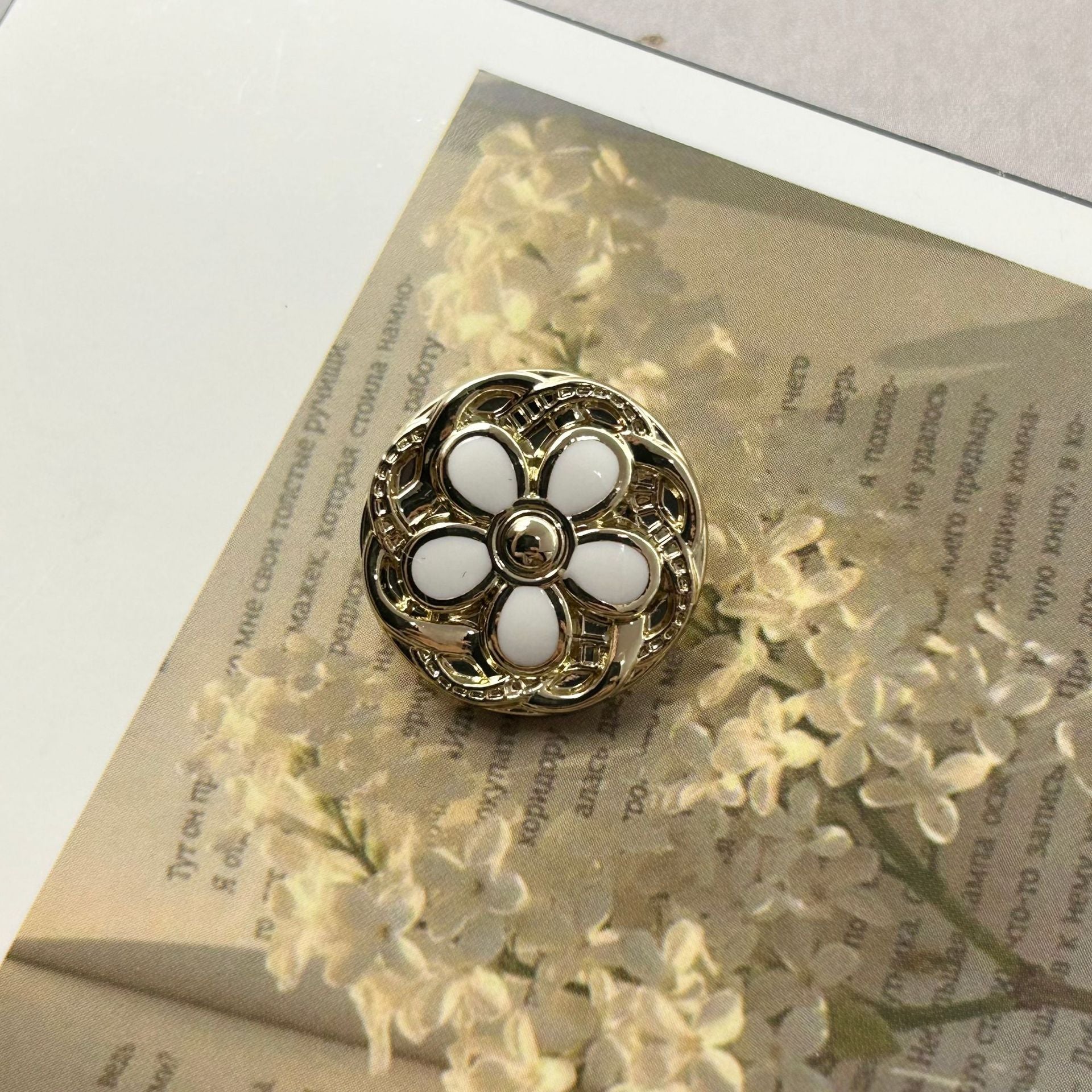 Round metal button, gold-tone floral lace design with white enamel petals