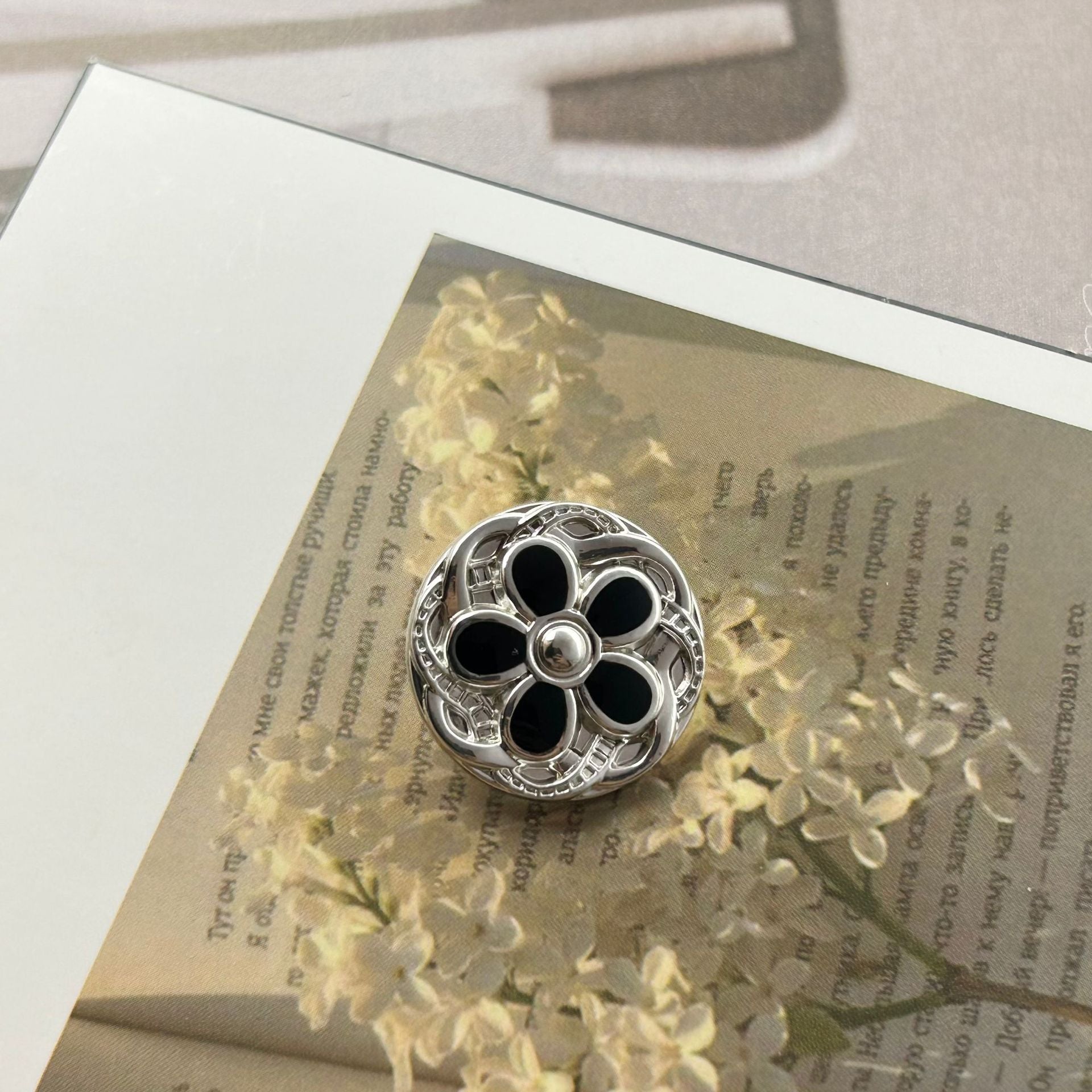 Round metal button, silver-tone floral lace design with black enamel petals