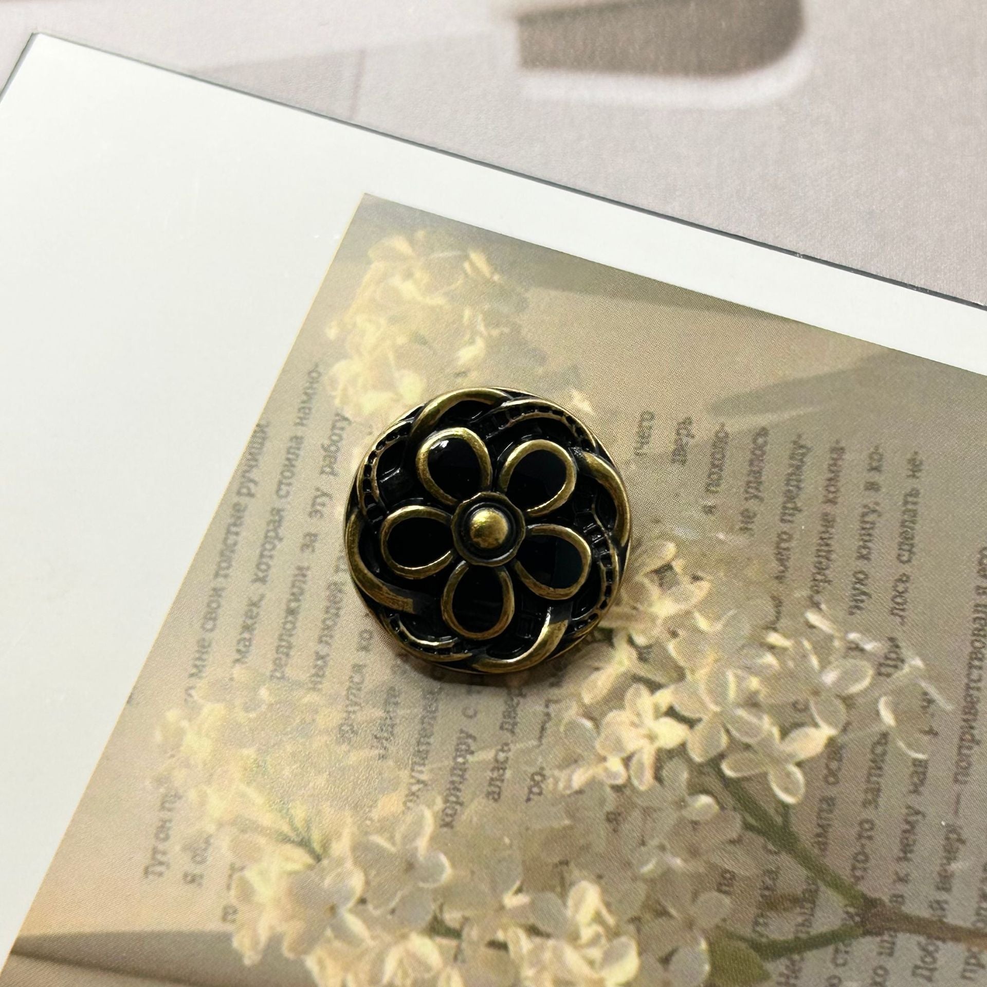 Round metal button, dark gold-tone with black enamel flower and gold edging
