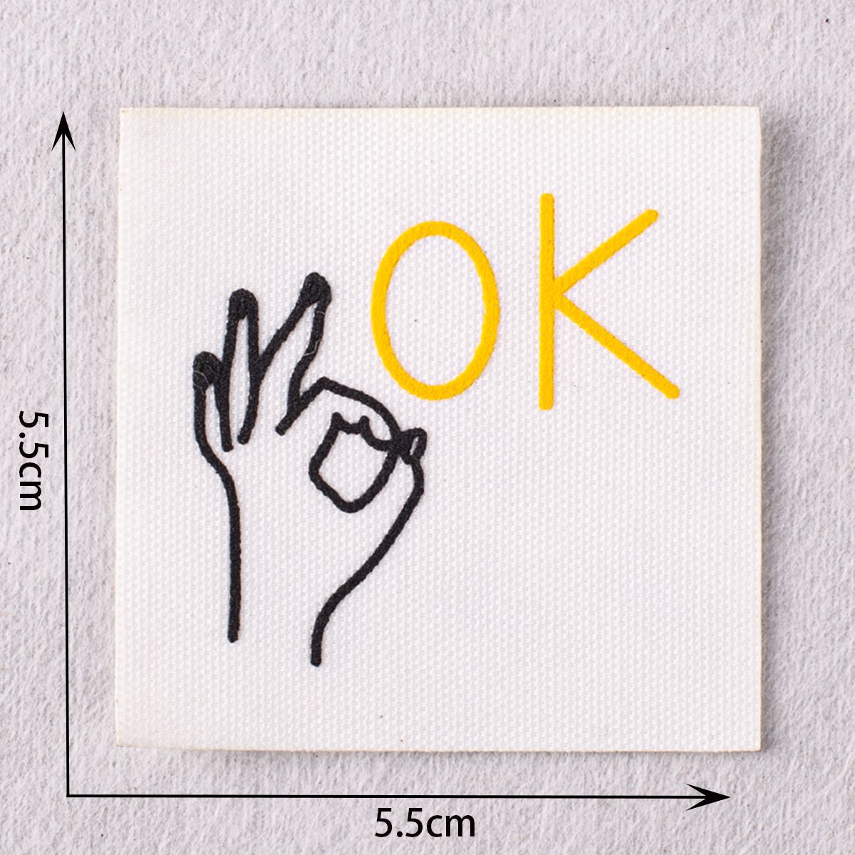 White stitched patch with yellow “OK” and hand sign