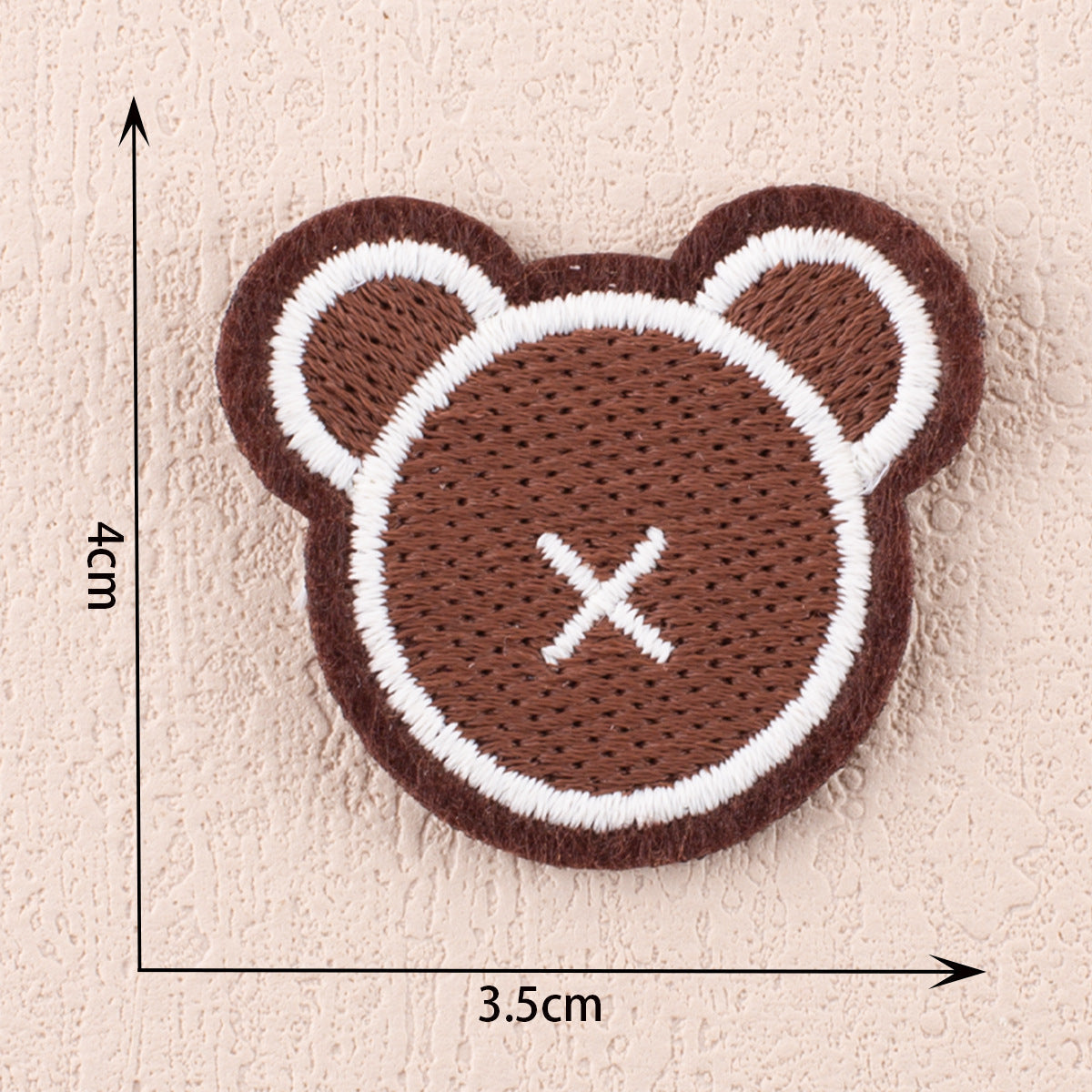 Brown teddy-bear letter patch with white embroidered X eyes and nose, size 3.5cm.