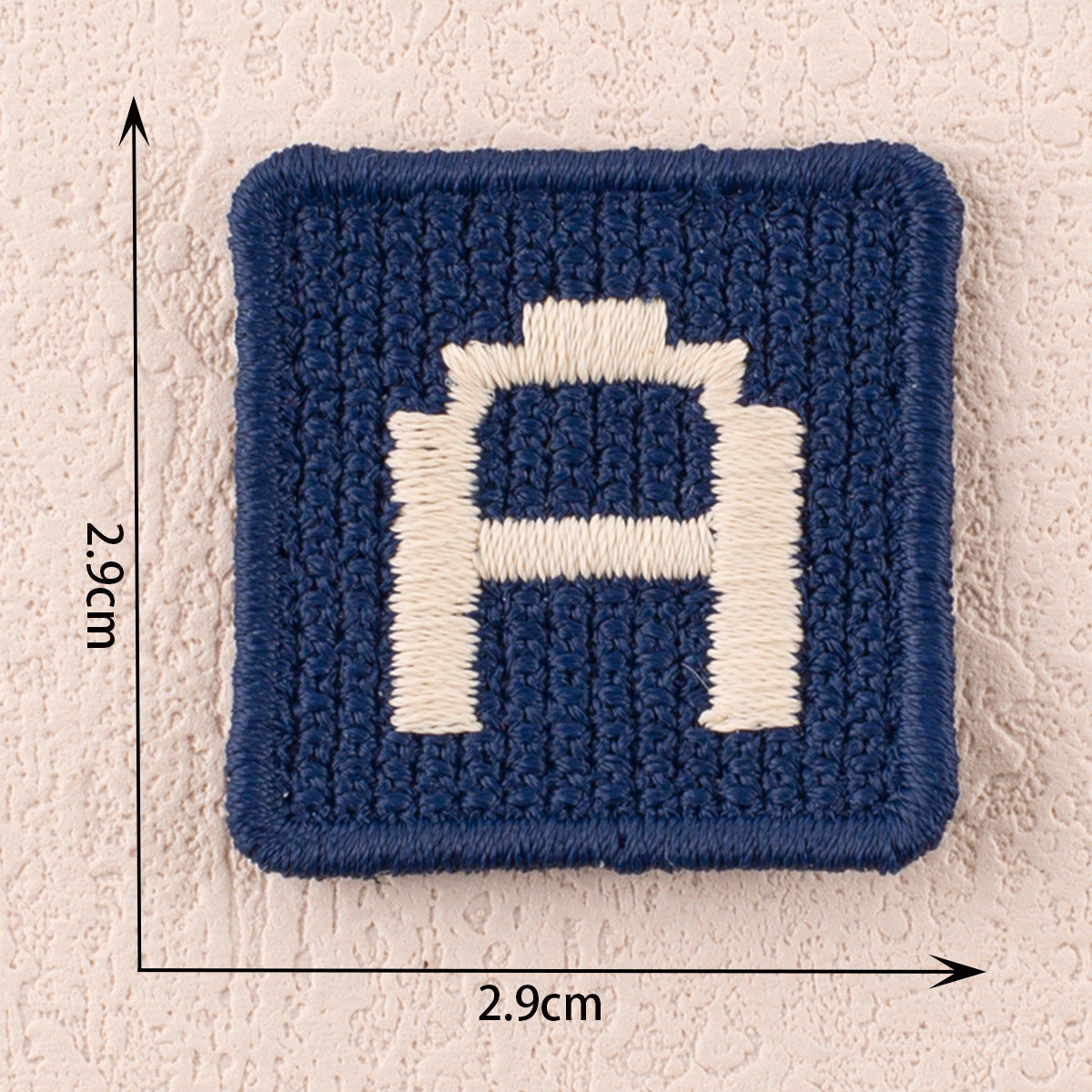 Blue fabric patch with white letter B, raised stitched edges, 2.9cm square.