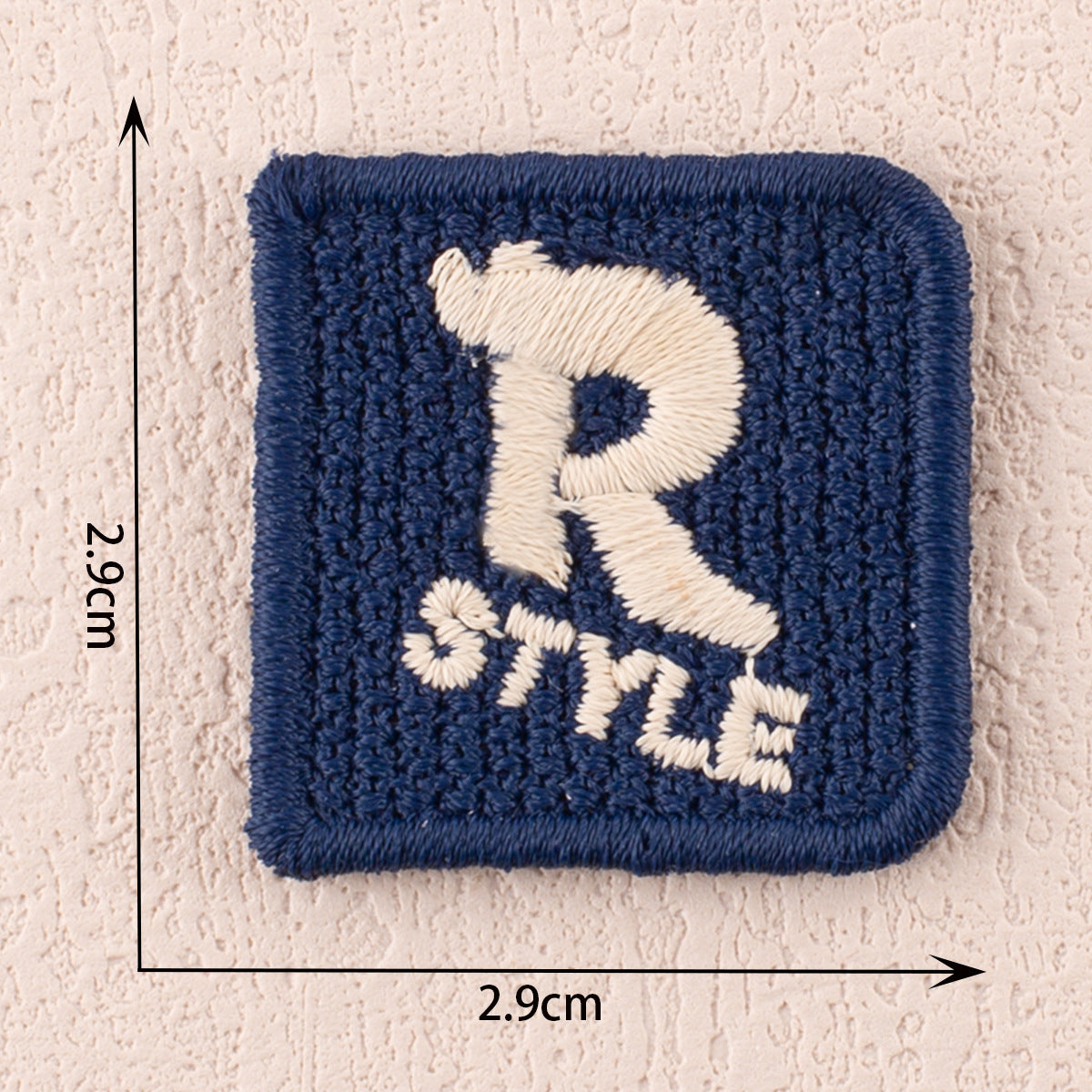 Blue fabric patch with white R-style letter and small stitched star accents, 2.9cm x 2.9cm.