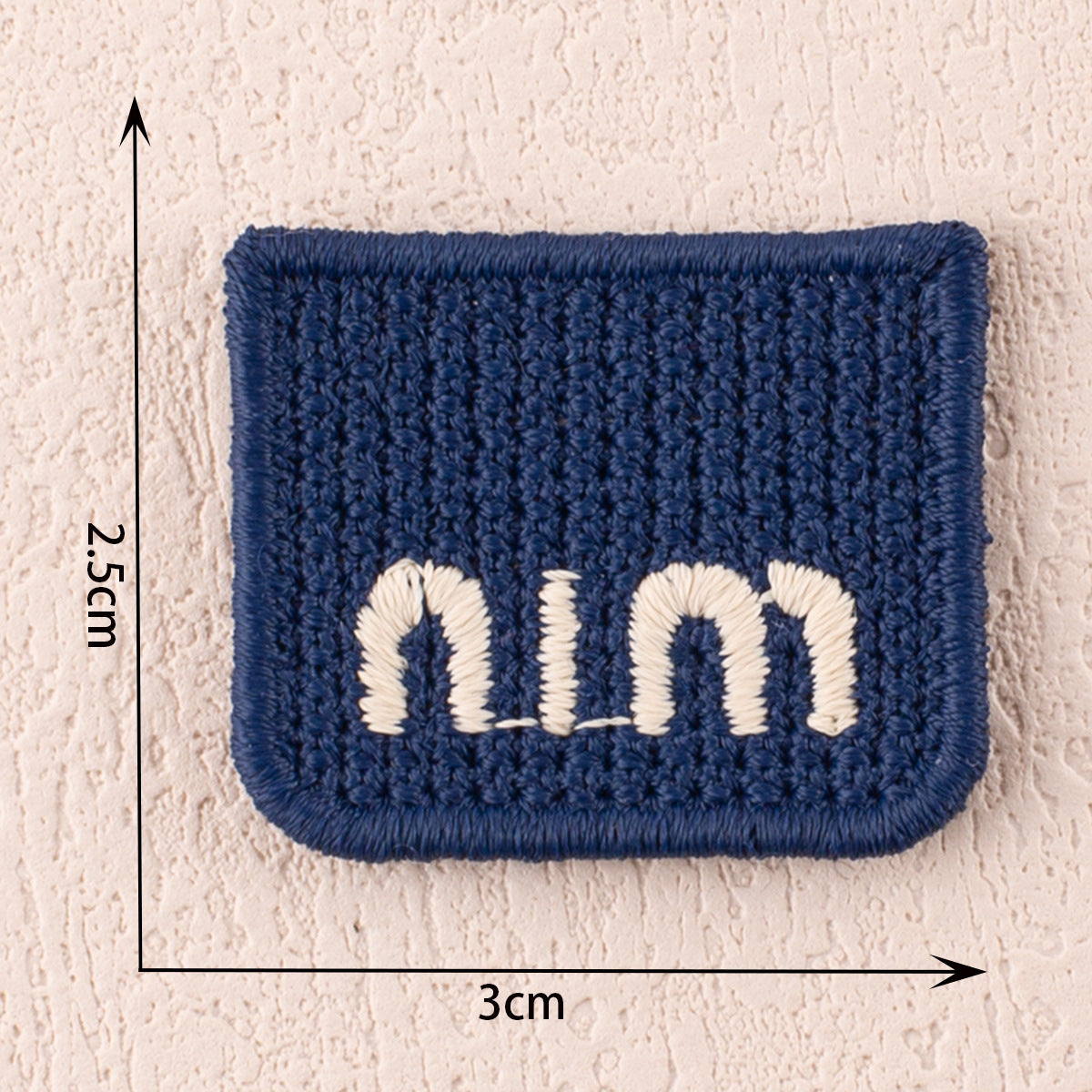 Blue fabric patch with white letter N, thick embroidered border, 3cm x 2.5cm.