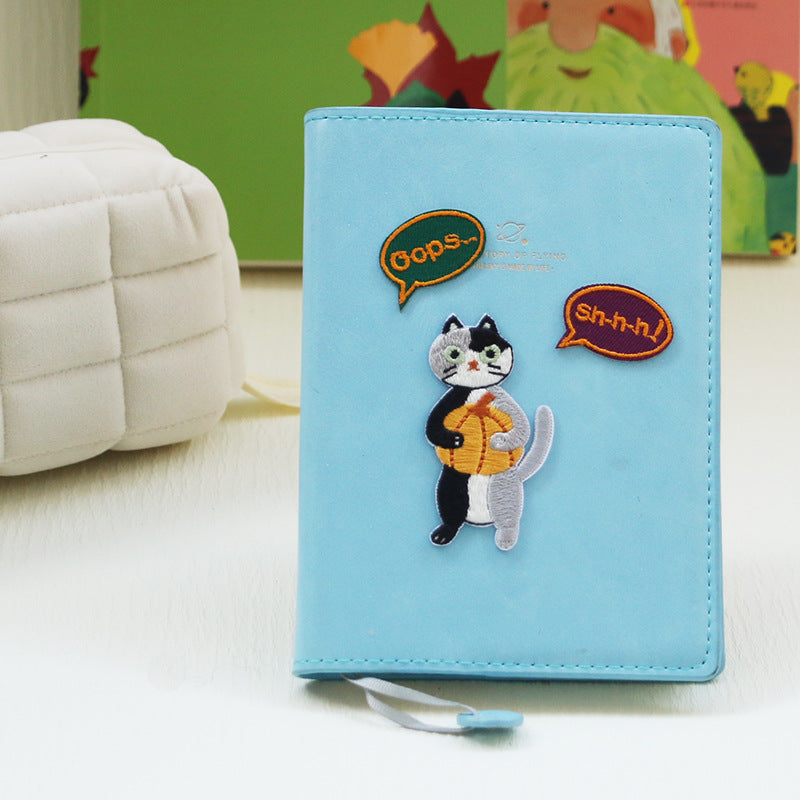 Self-adhesive embroidered cat patch on light blue wallet, holding a yellow pumpkin bag
