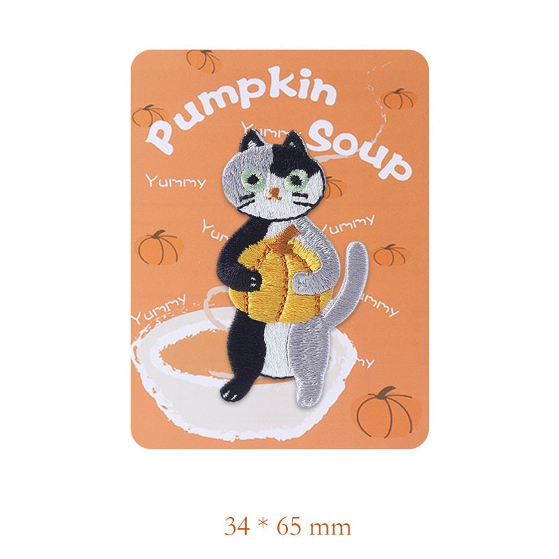 Embroidered black-and-white cat patch holding a spoon, wearing a yellow apron