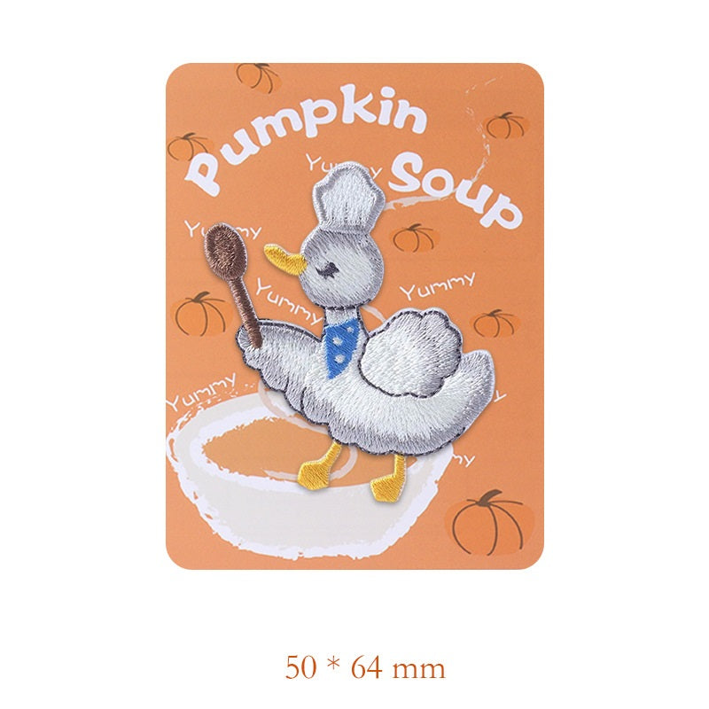 Embroidered grey duck patch holding a spoon, blue bib with musical notes