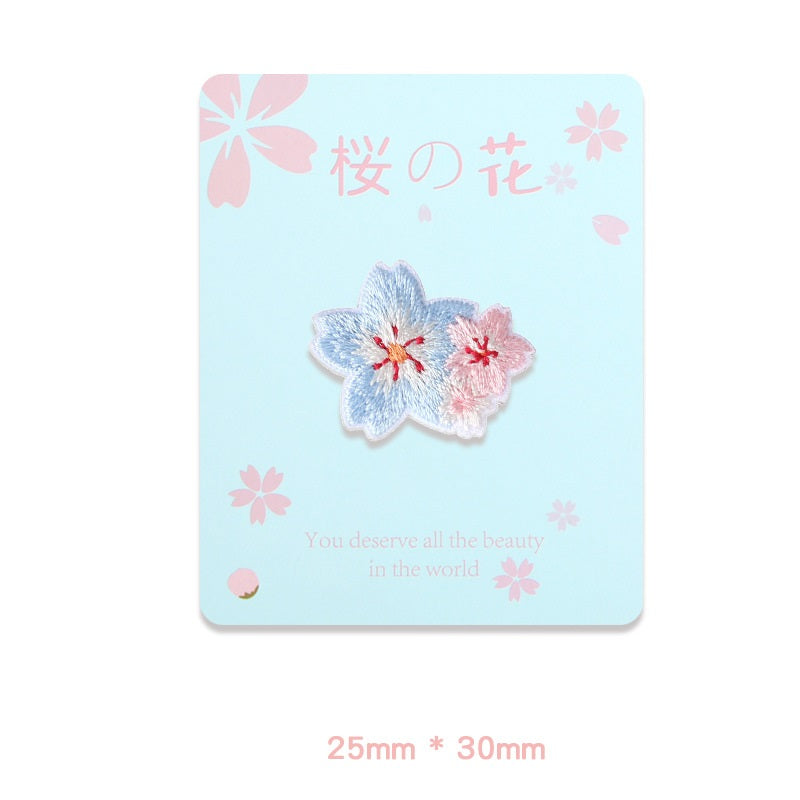 Pair of embroidered sakura flowers: blue with red centers and pink with soft sheen