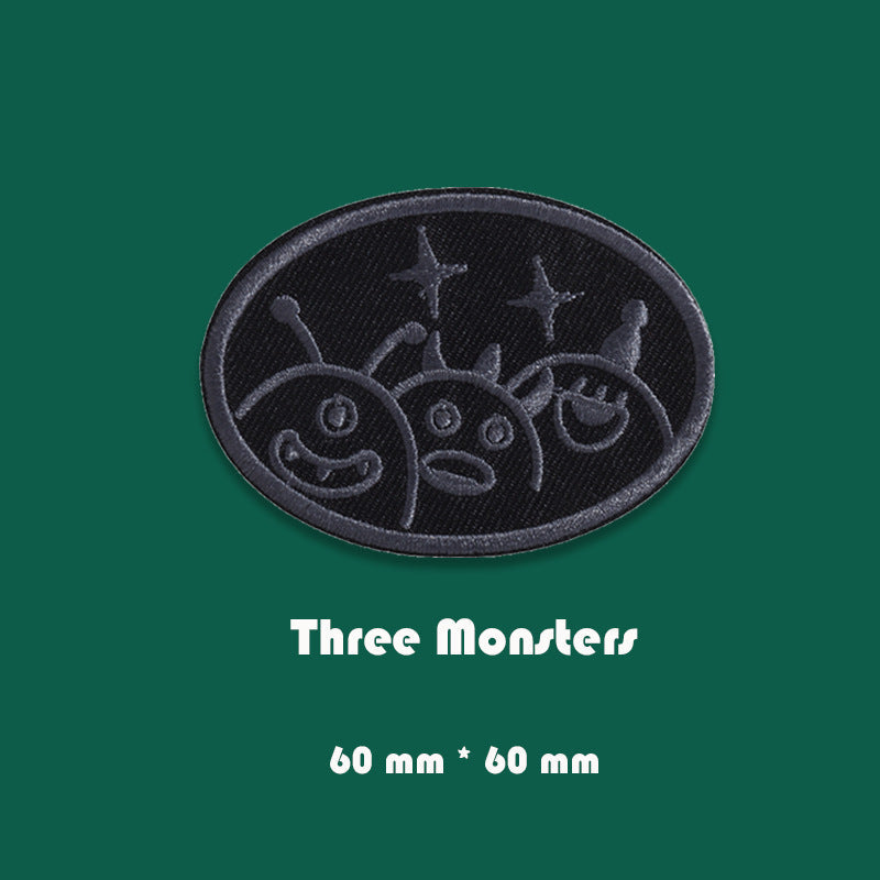 Black embroidered badge patch showing three monster faces, 60mm x 60mm