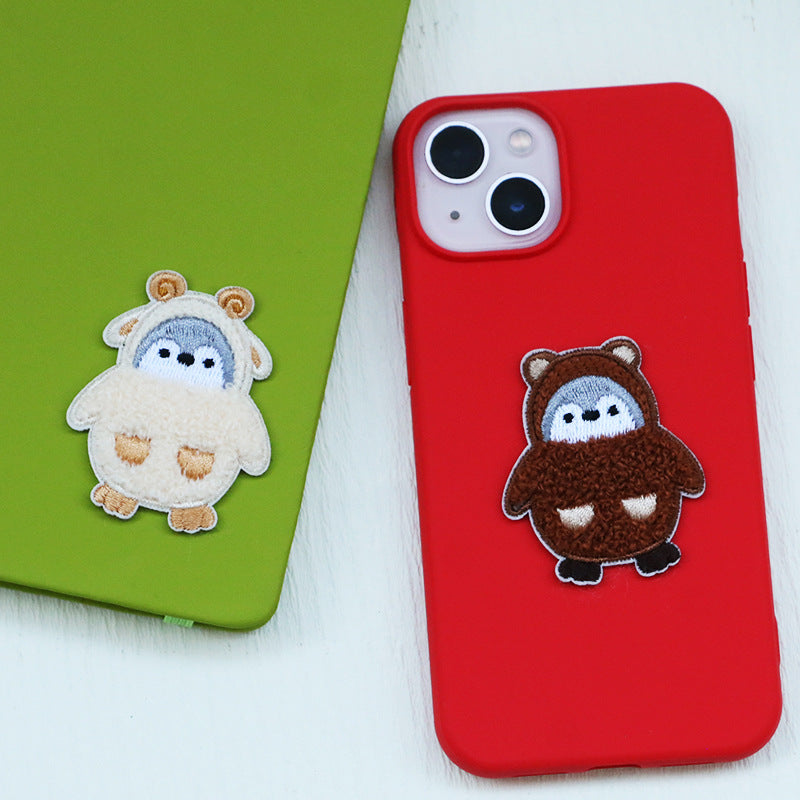 Flauschiger Pinguin-Patch, braun mit grauem Gesicht, am roten Handycover