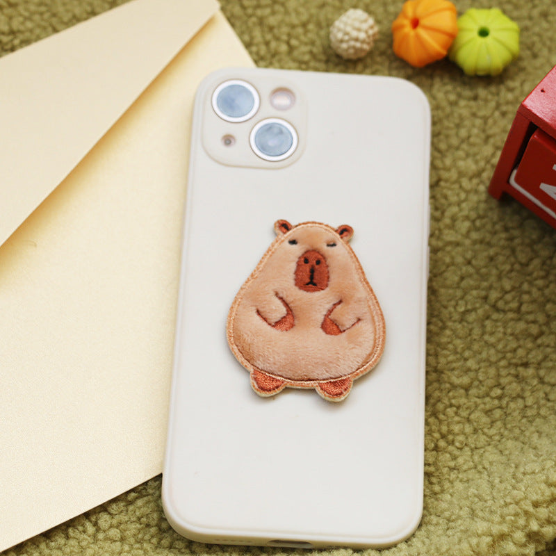 Brown and tan capybara embroidered self-adhesive patch on phone case, bear paws up.