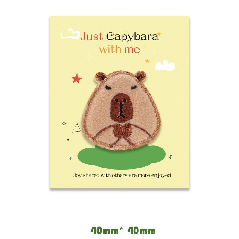 Brown capybara embroidered self-adhesive patch, smiling face with paws folded.