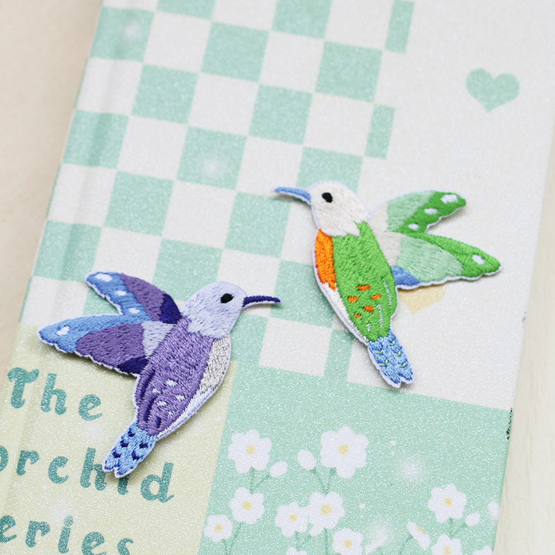 Self-adhesive hummingbird embroidered patches in purple-blue and green on light fabric