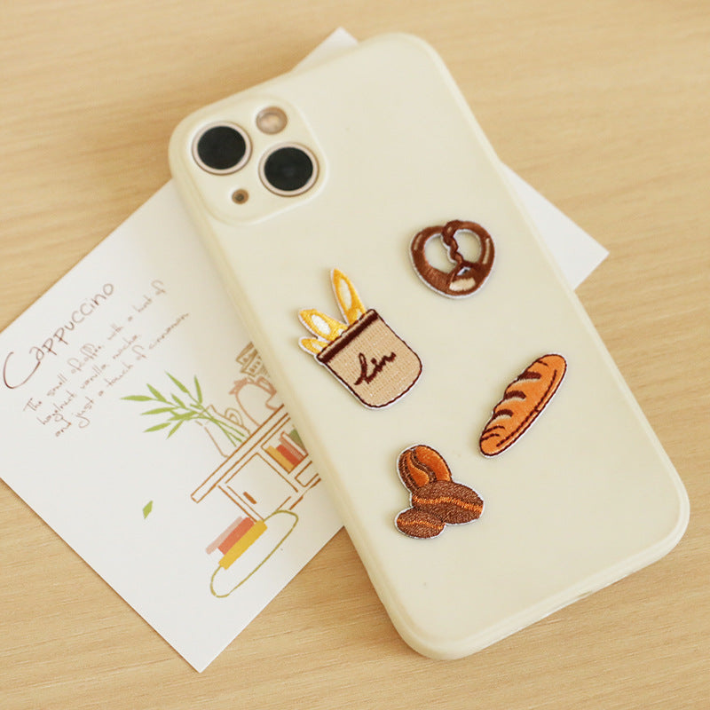 Mini embroidered baking patches on phone case: pretzel, crock-pot bun, coffee cup, baguette, bunny.