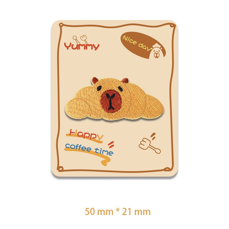Gesticktes Capybara-Patch, braune liegende Figur mit schwarzem Gesicht und roter Nase