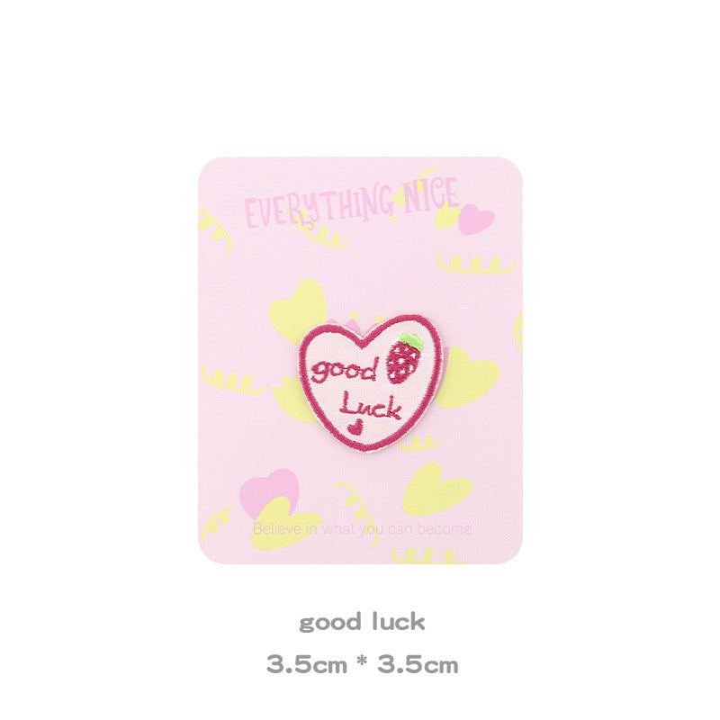 Pink heart-shaped patch embroidered “Good Luck” with strawberry-style pattern in the center