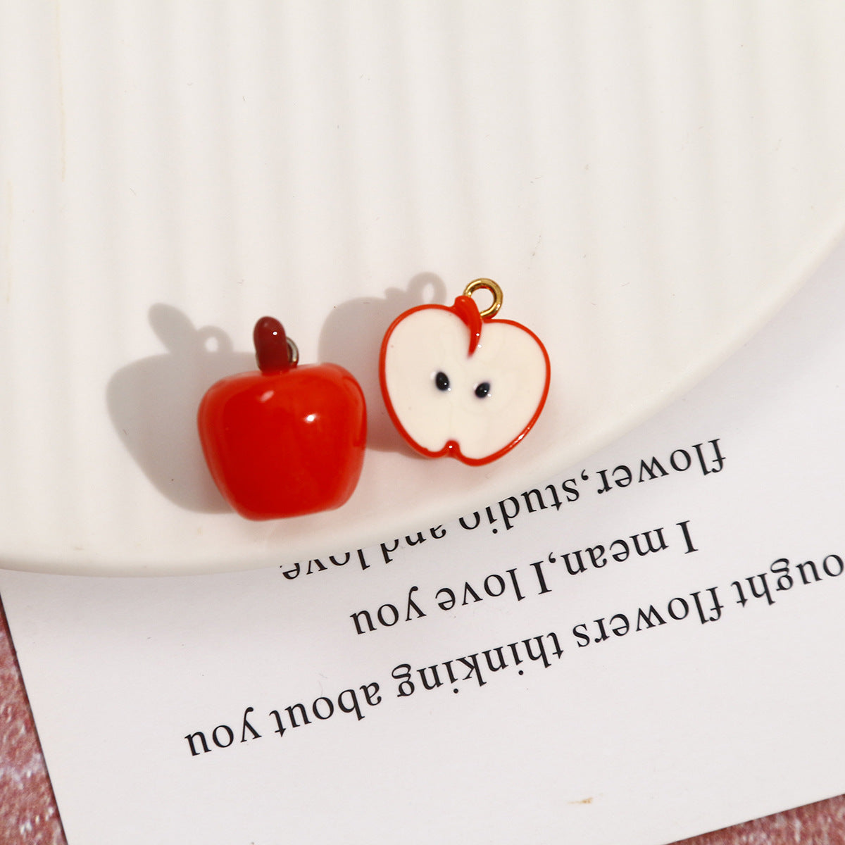 Orange-red apple resin pendant pair: one whole apple and one cut half with cartoon face