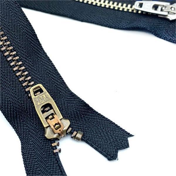YKK metal closed-end zipper close-up: dark-navy tape with brass puller and teeth